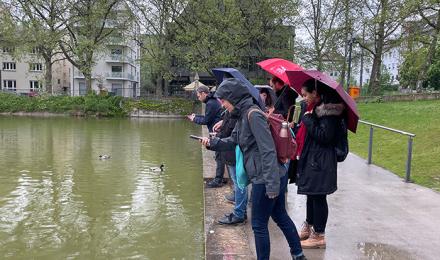 Wasserqualität monitoring, Gruppe steht am Gewässer und fotografiert das Wasser